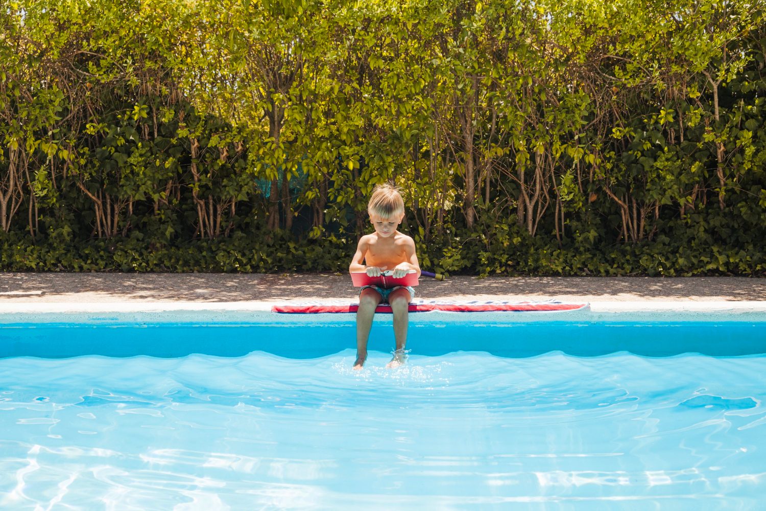 Young child sitting at the edge of a sunny backyard swimming pool